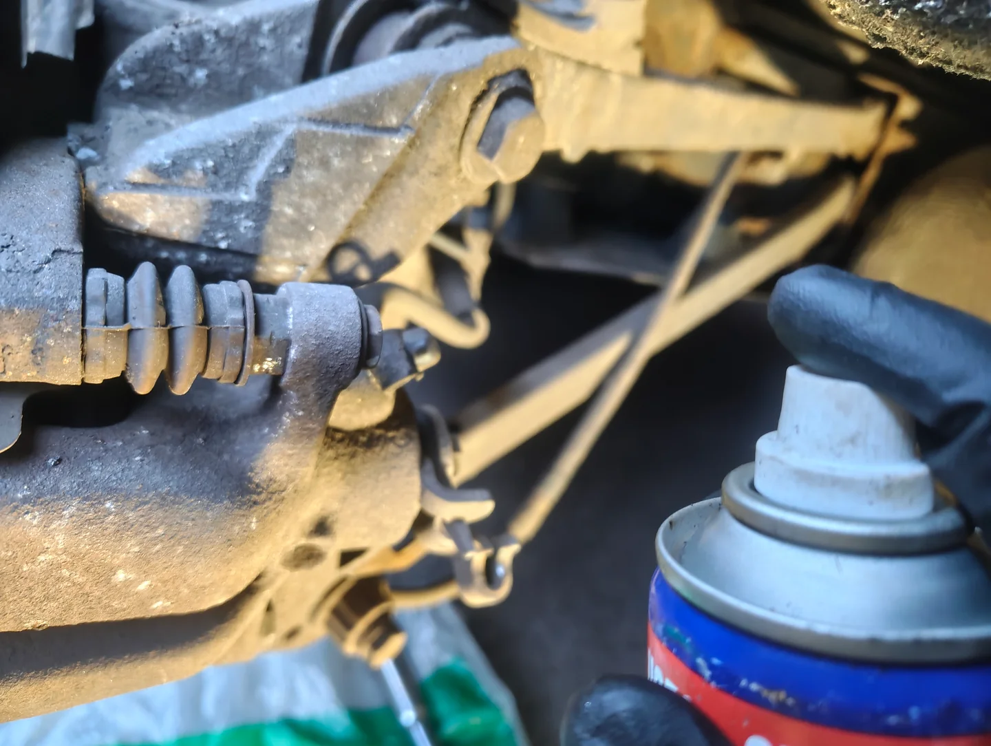 Spraying penetrant on the top and bottom brake caliper slider pin fixing bolts.